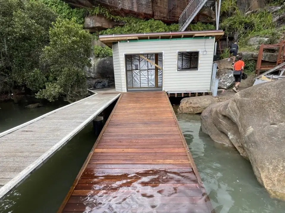 A jetty running up a steep rocky block to a boat shed under construction, with the crew working on site