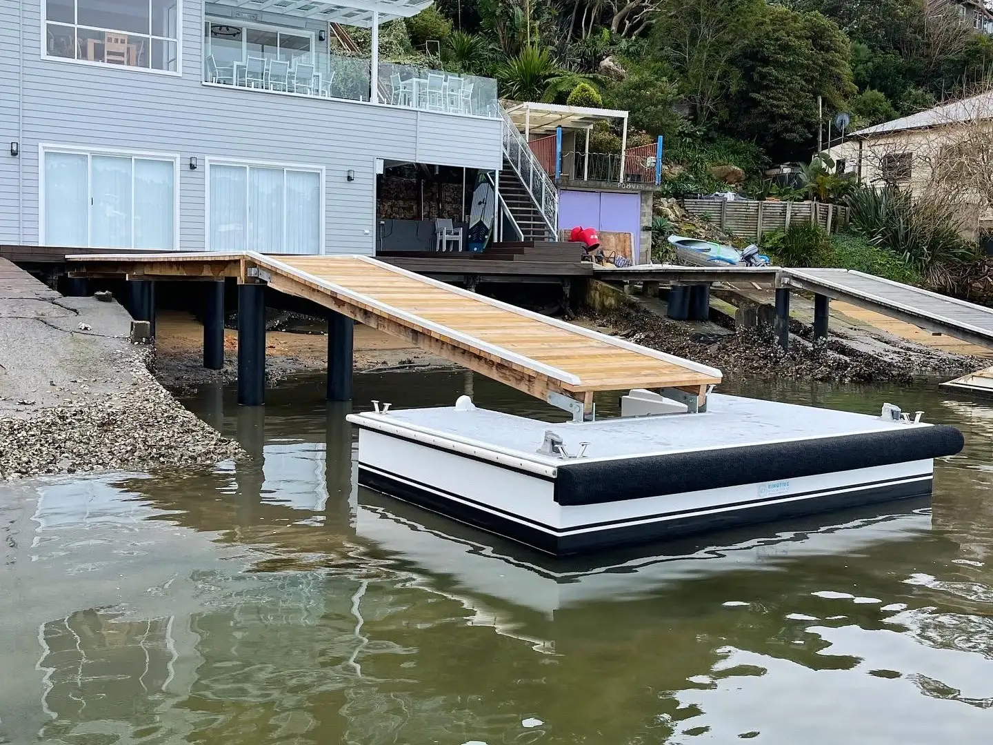 A waterfront house with its jetty and pontoon rebuilt across the rock foreshore below it