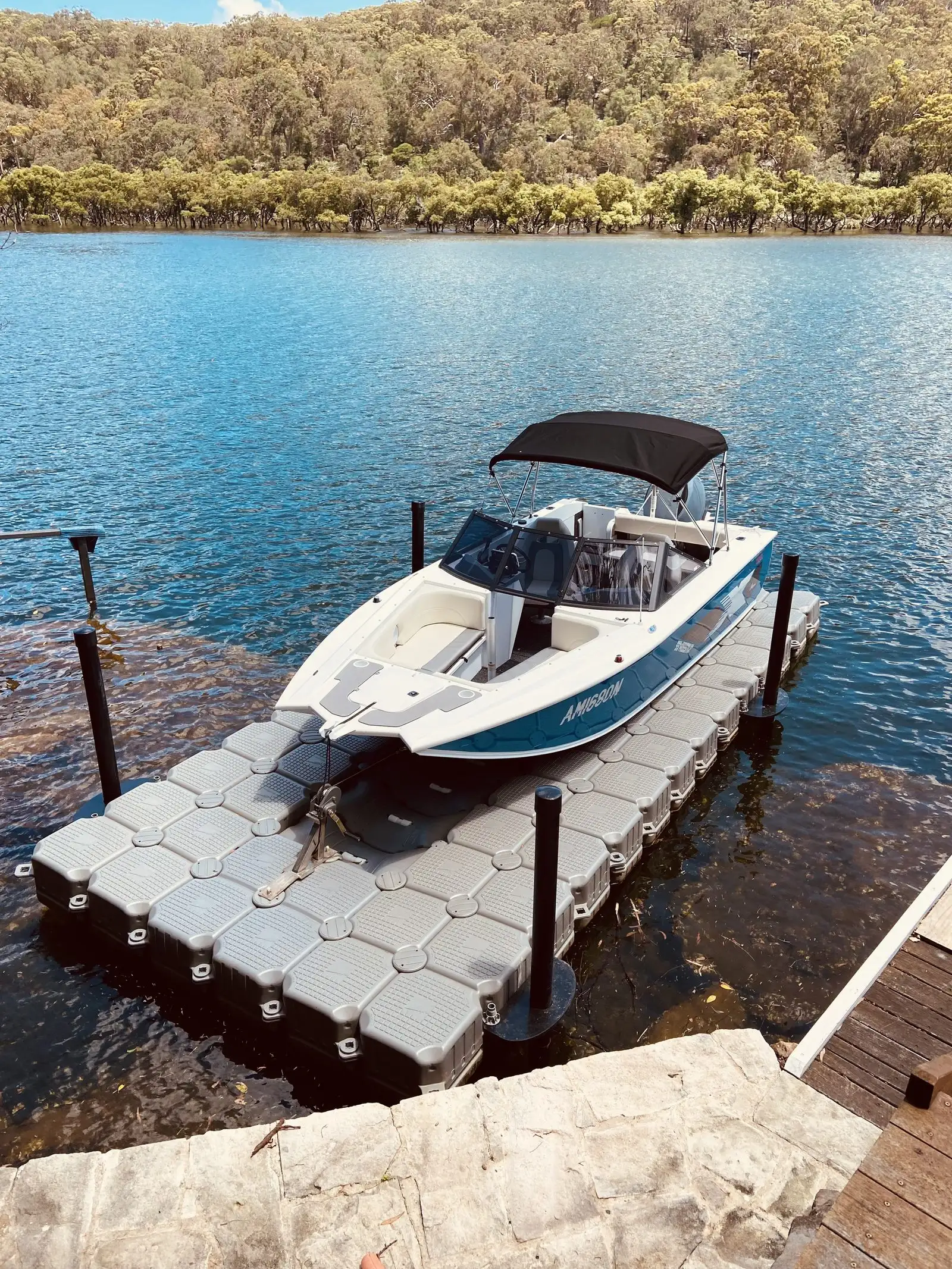 Runabout driven up onto a grey modular floating dock with its hull sitting clear of the water