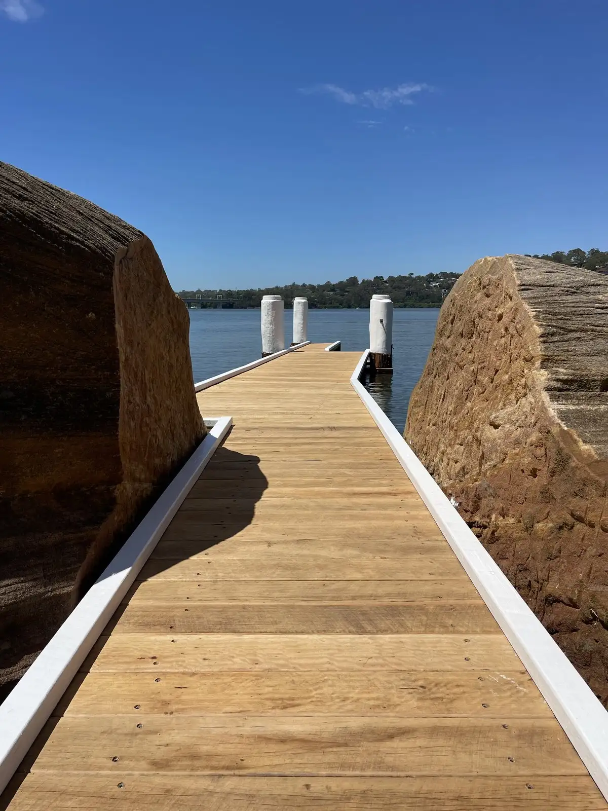 Freshly laid hardwood jetty deck running between two large sandstone boulders out to capped white piles on the river