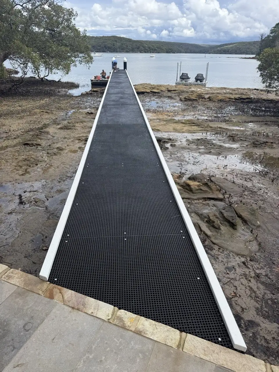 Open-mesh jetty walkway crossing a rocky foreshore at low tide
