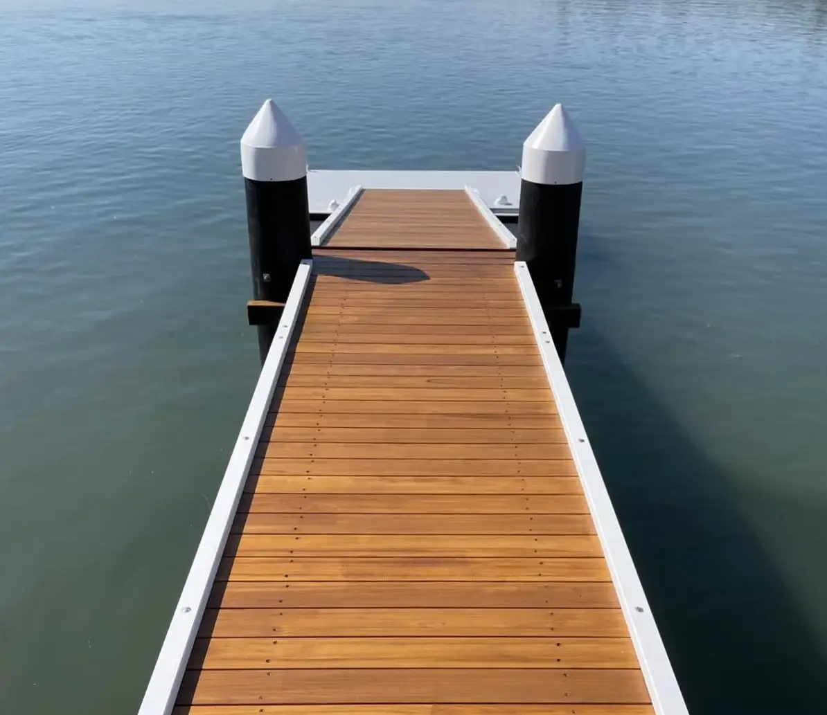 Freshly oiled hardwood jetty decking leading between two capped black mooring piles to a gangway