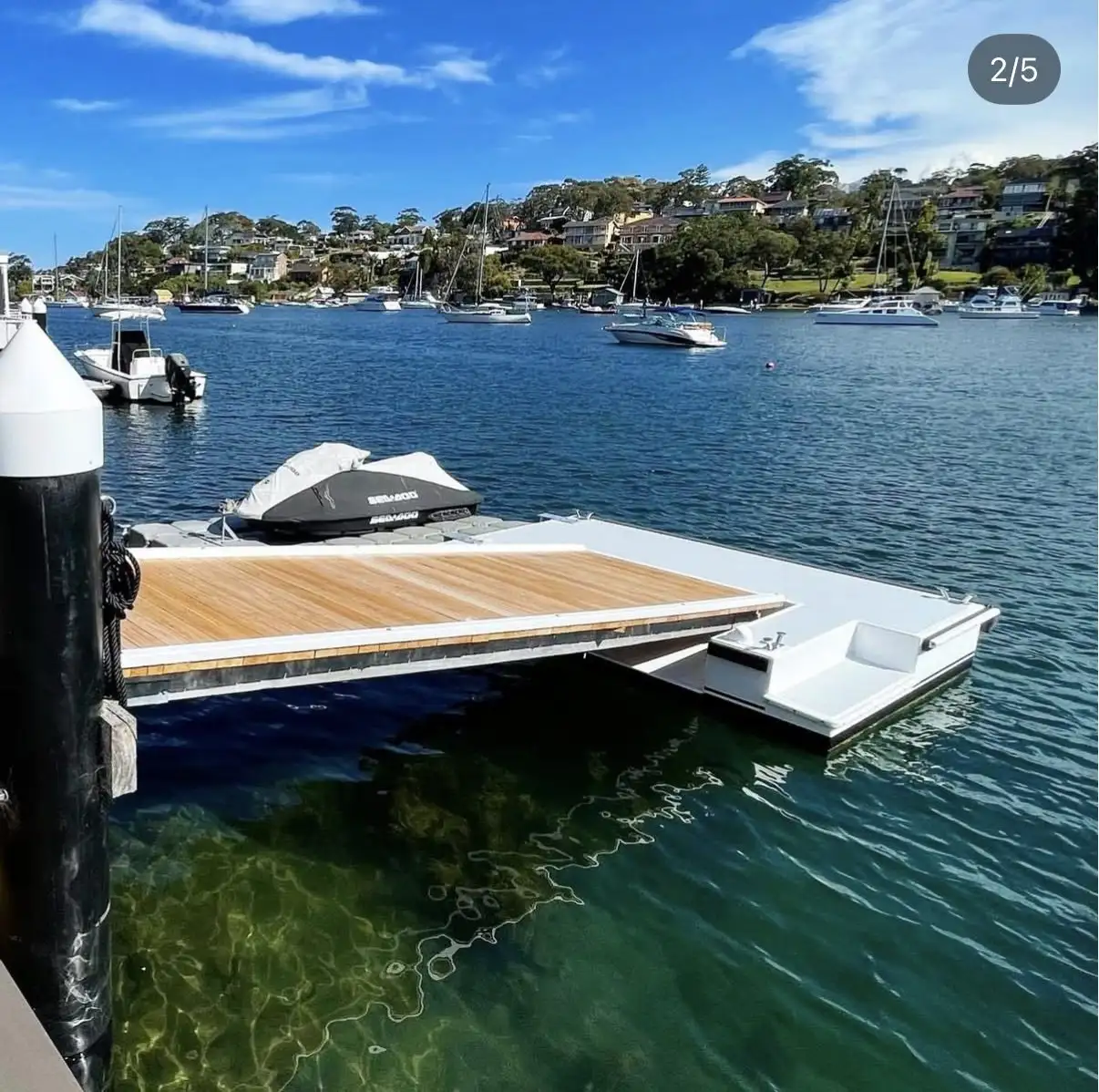 Hardwood-decked floating pontoon rising with the tide beside a jetty, with a jet ski berthed alongside