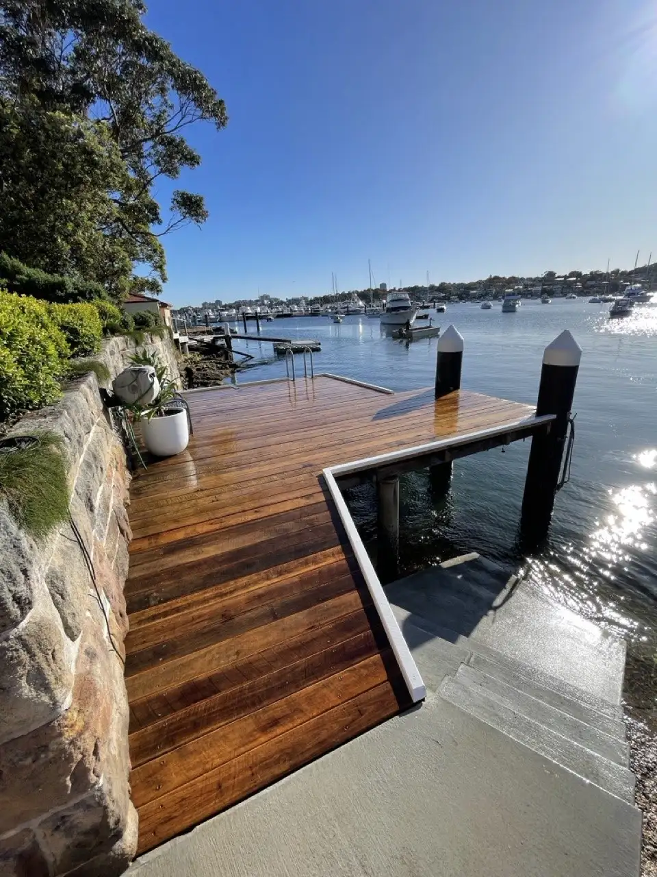 Hardwood jetty deck beside a sandstone wall, with the moored fleet behind
