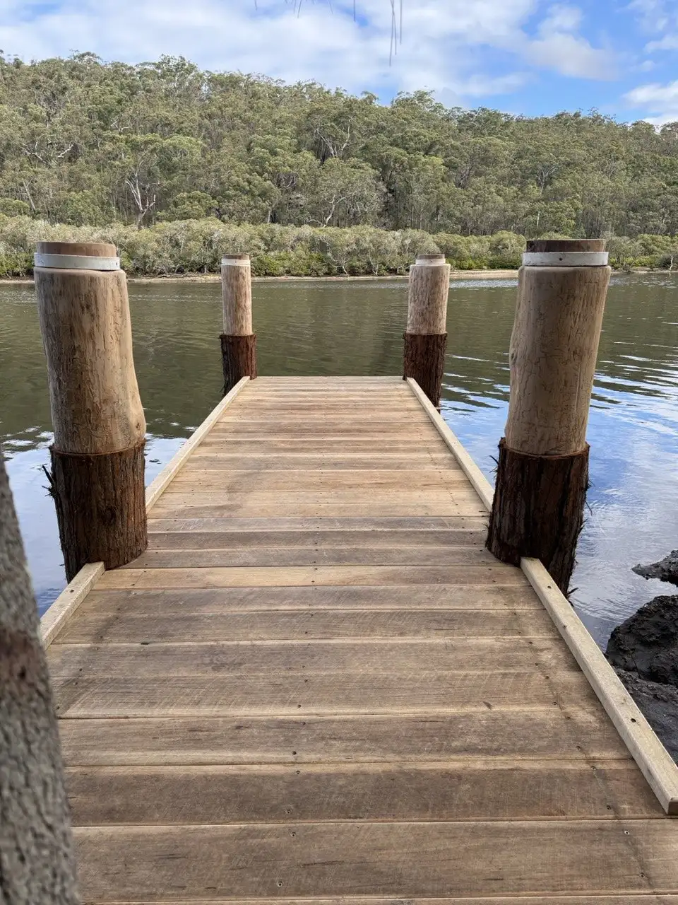 Hardwood jetty deck running between four capped timber piles to the water