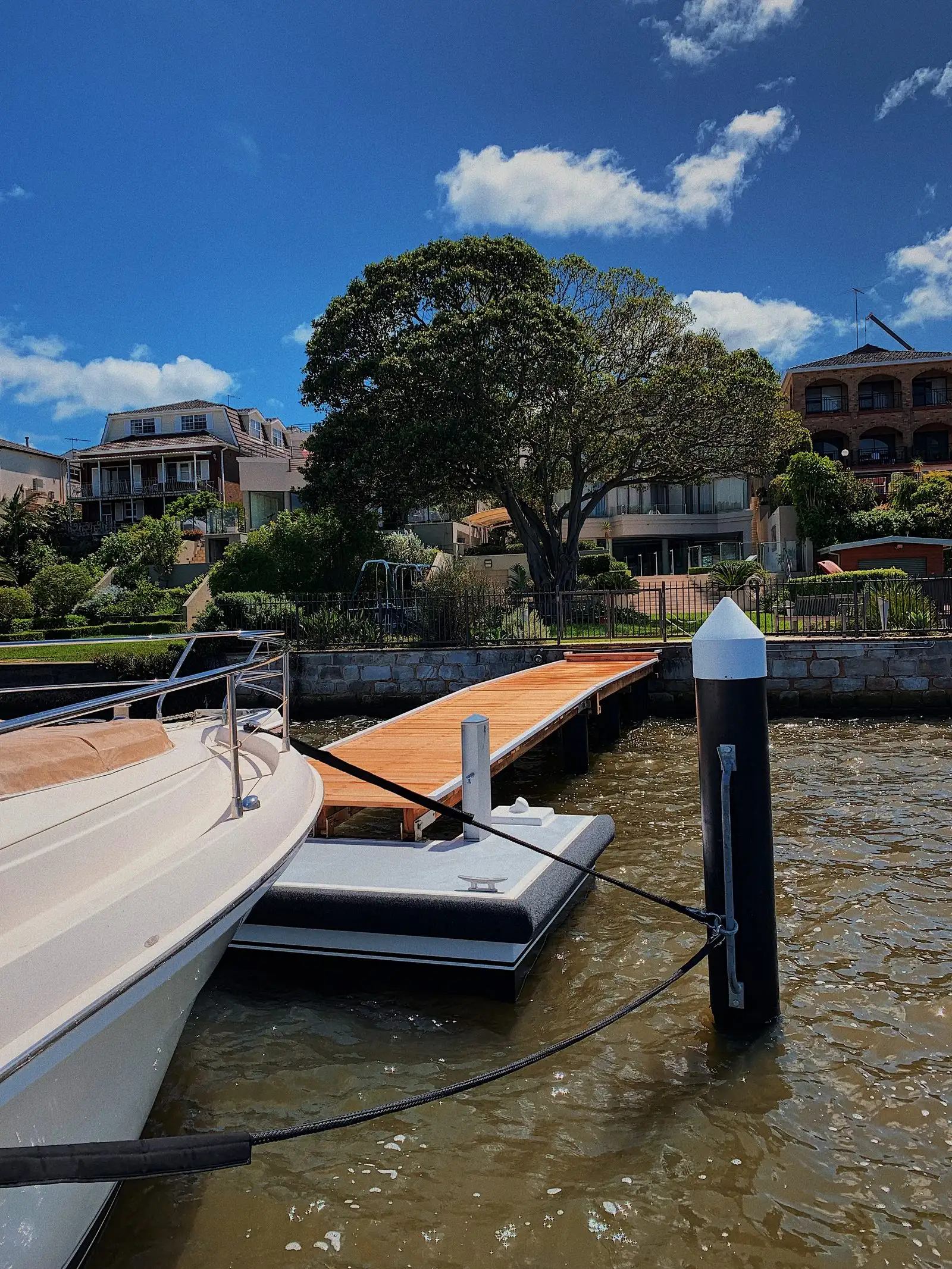Cruiser moored against a Kingtide Marine pontoon held off the seawall by a capped guide pile, with a hardwood gangway running back to the garden