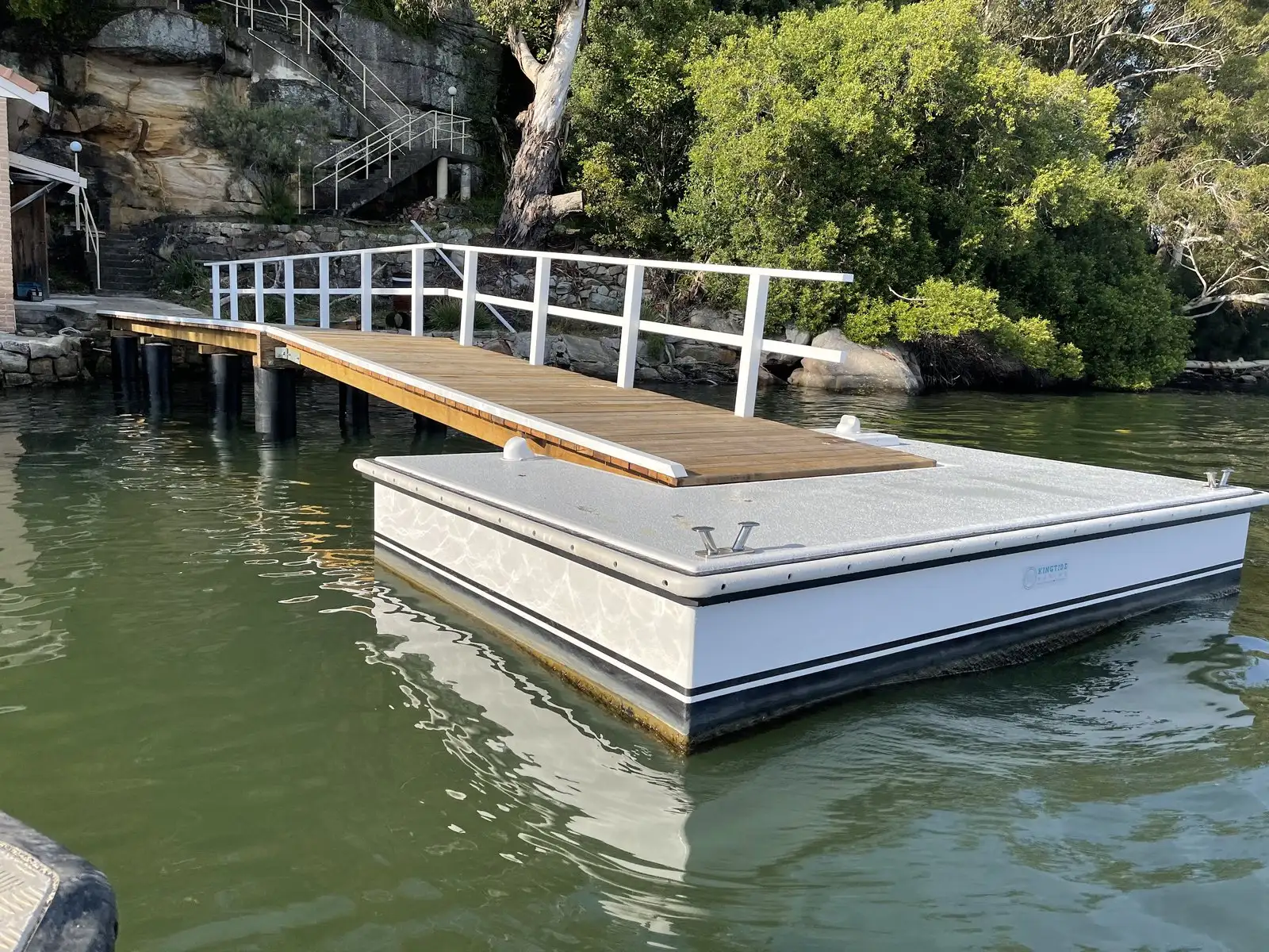 A Kingtide Marine pontoon floating level with the tide at the foot of its hardwood gangway, against a rocky foreshore
