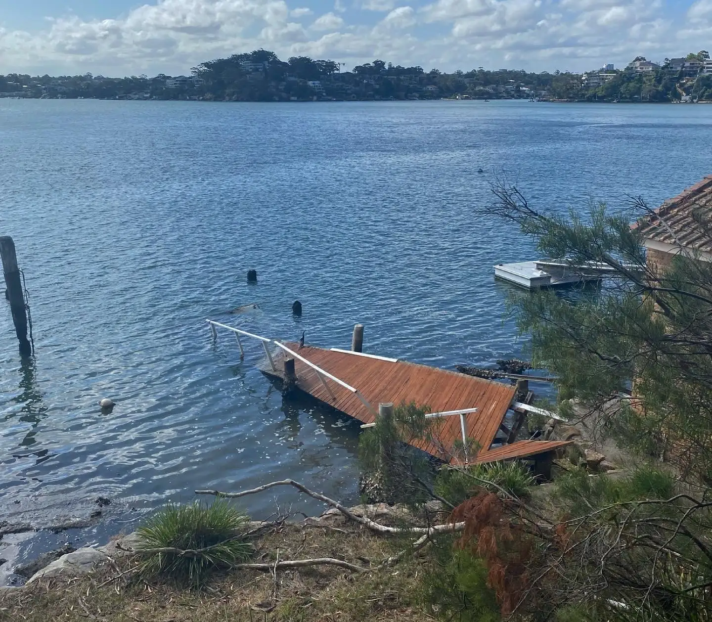 A jetty collapsed into the water after storm damage, boards adrift on the foreshore