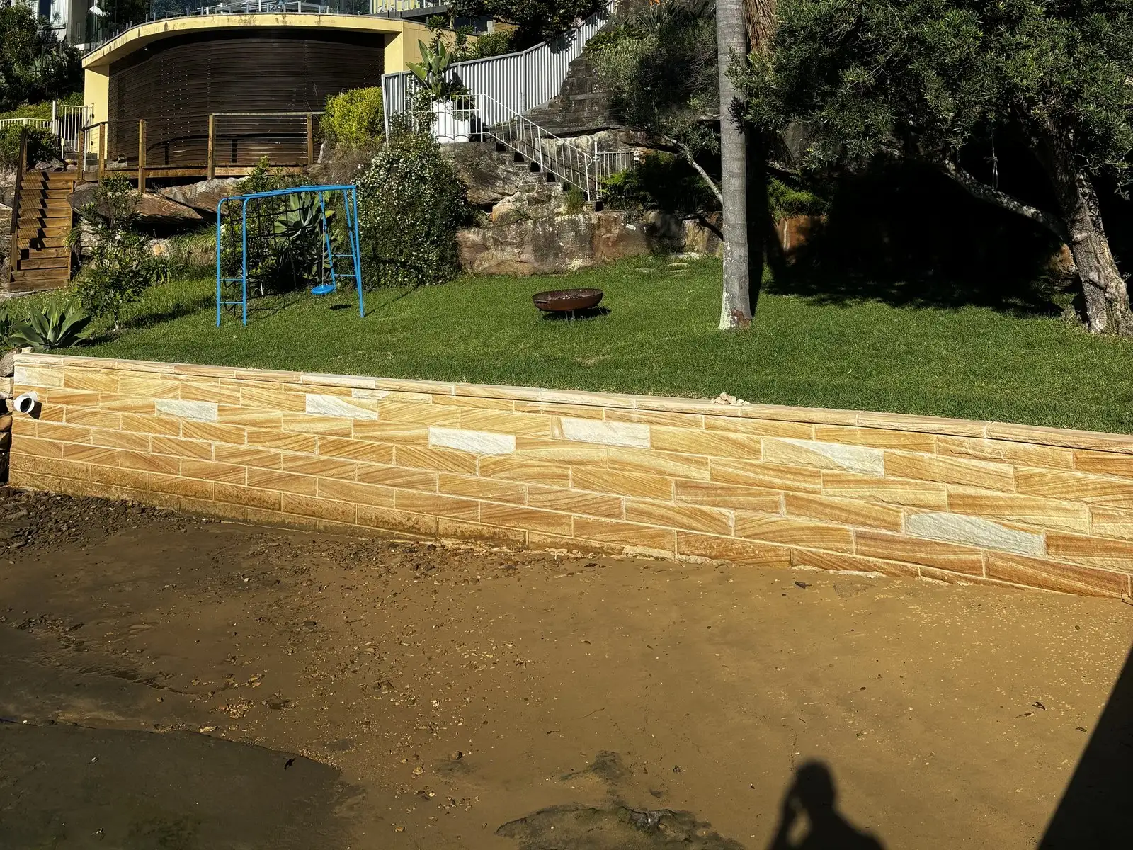 A newly built sandstone seawall running the width of a waterfront lawn down to the sand