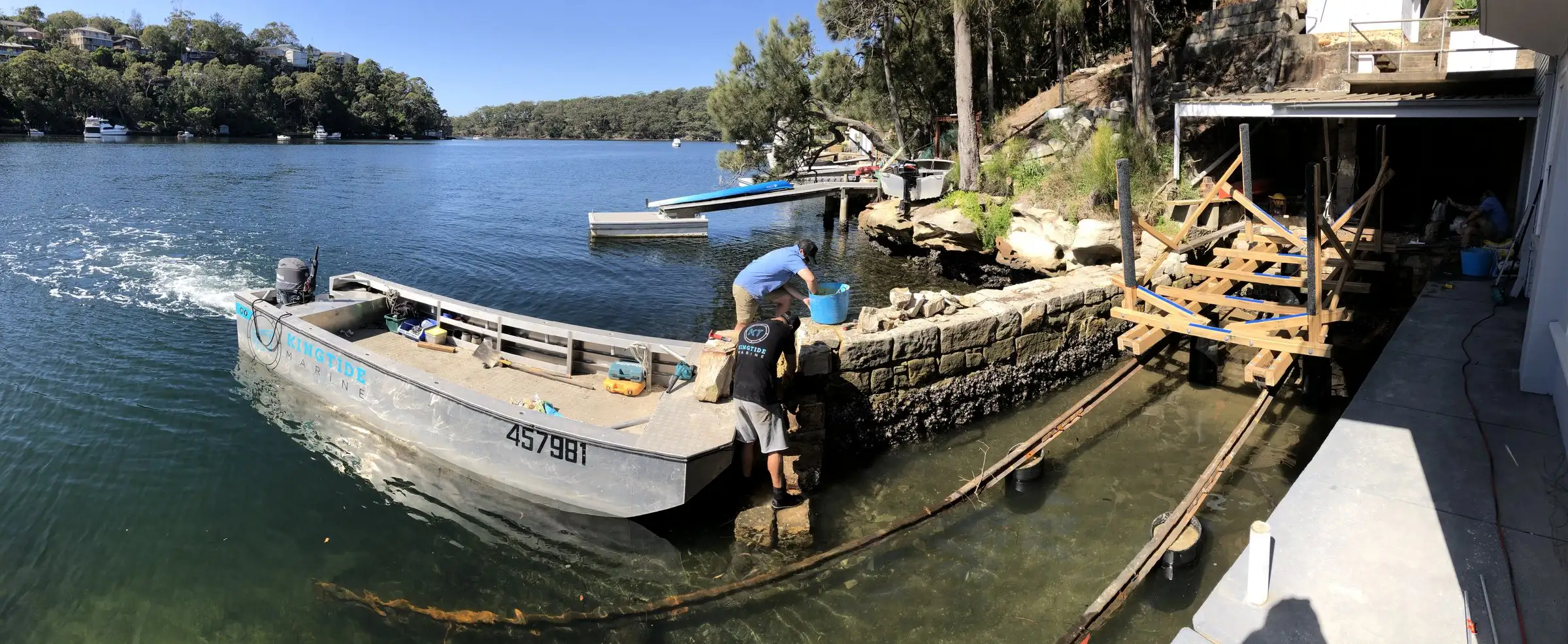 Kingtide Marine crew working from a punt alongside a sandstone seawall under construction, with the timber formwork still in place