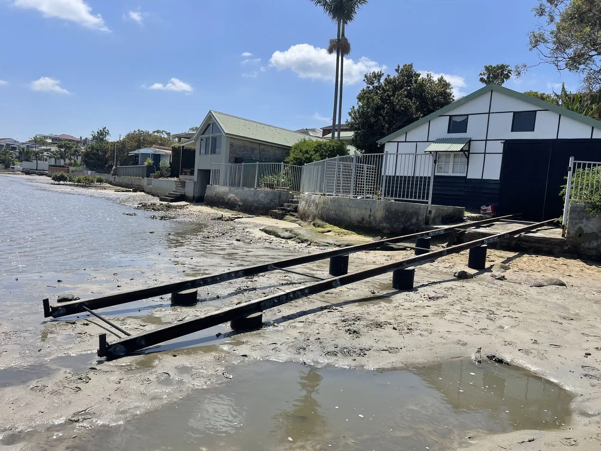 Slipway rails running down the sand and into the water beside a waterfront boat shed