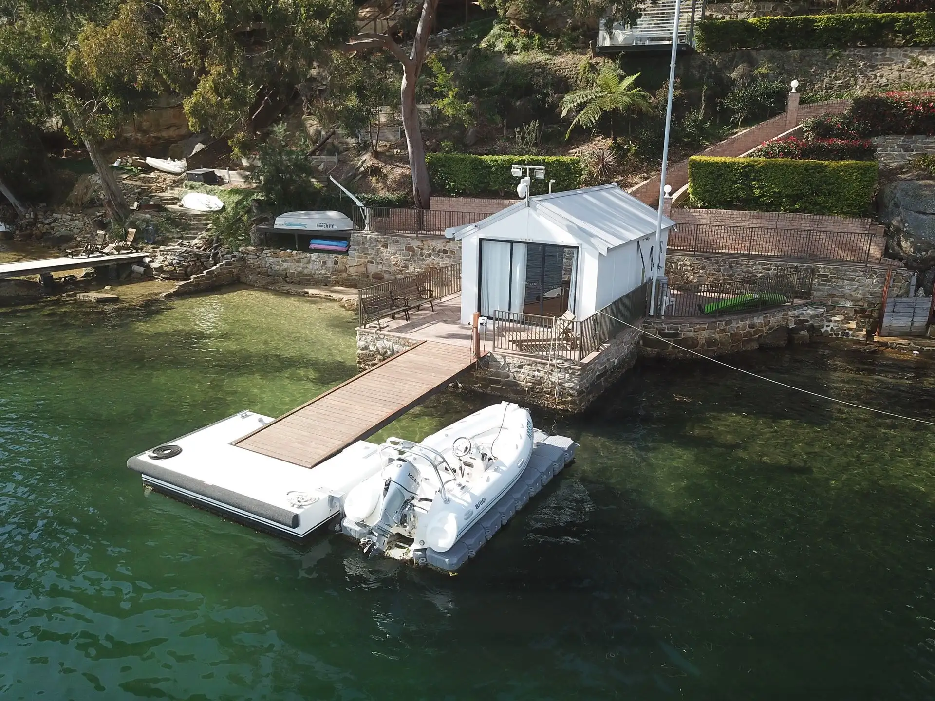 Waterfront boat shed with a timber jetty and floating dock in front of it on a Sydney foreshore