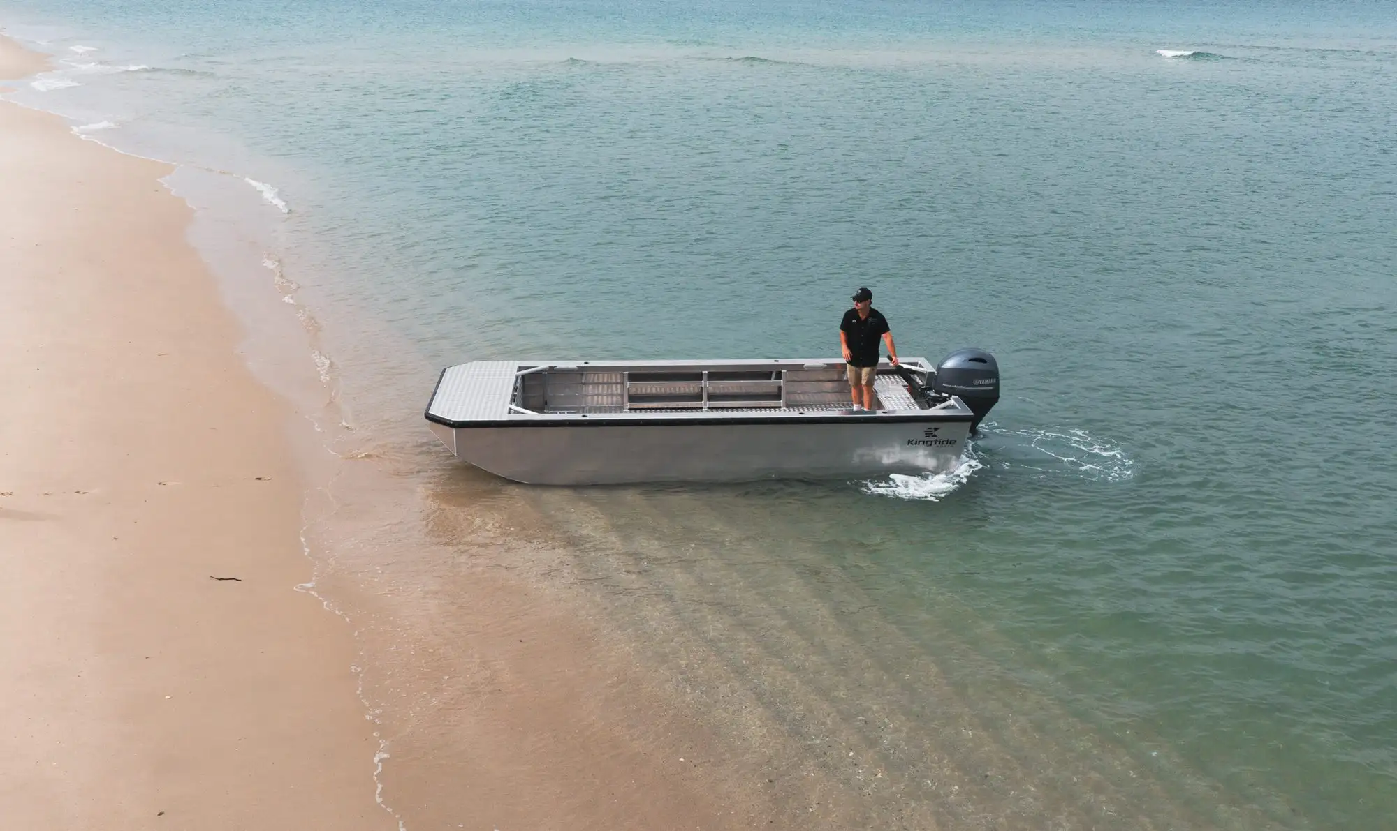 Kingtide Marine aluminium work boat nosed onto a shallow sand beach with the operator aboard